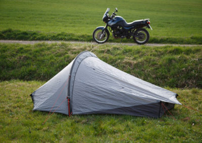 Das Zelt im Vordergrund auf einer Wiese, das Motorrad im Hintergrund