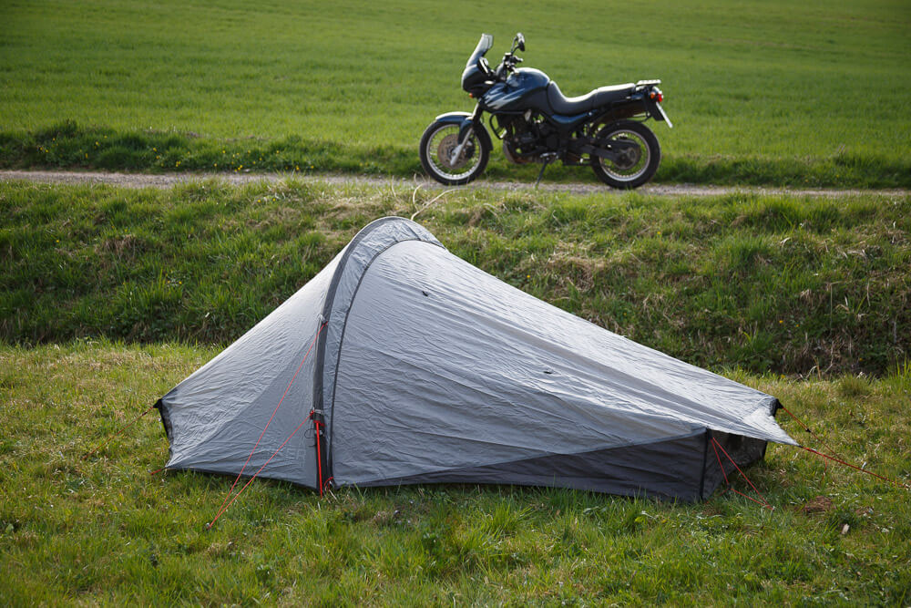 Das Zelt im Vordergrund auf einer Wiese, das Motorrad im Hintergrund