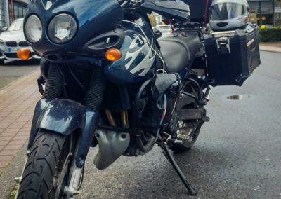 Triumph Tiger mit bei der ein Satz Reifen auf das Topcase gespant wurde.