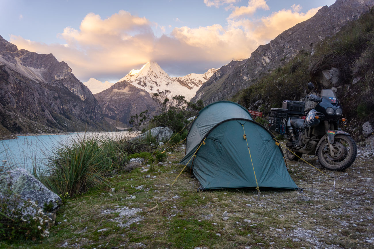 Motorcycle and tent in front of a mountain lake